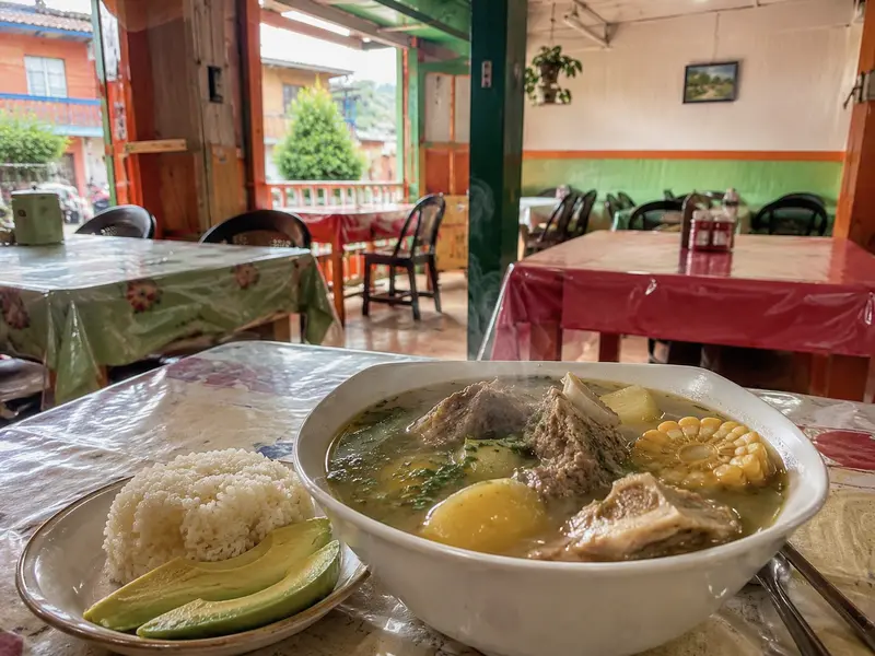 Bowl of sancocho with rice and avocado in a simple local Colombian comedor